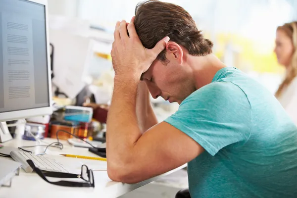 Hombre estresado trabajando en el escritorio en la oficina creativa ocupada — Foto de Stock