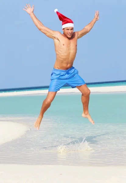 Hombre saltando en la playa usando sombrero de Santa — Foto de Stock