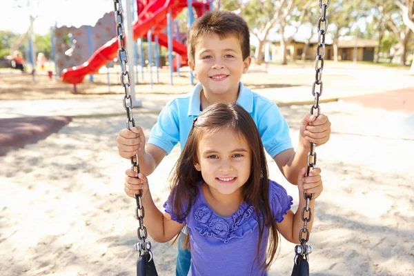 Chico y chica jugando en swing en parque —  Fotos de Stock