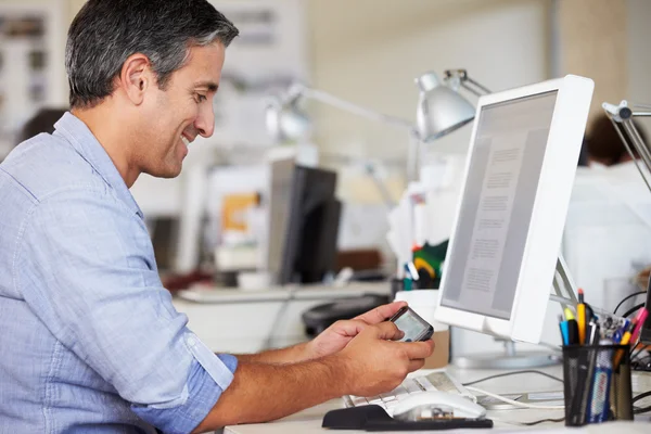 Uomo che utilizza il telefono cellulare alla scrivania in ufficio creativo occupato — Foto Stock