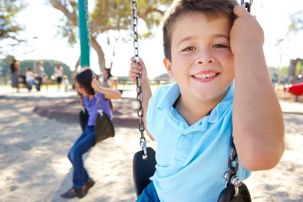 Chico y chica jugando en swing en parque —  Fotos de Stock