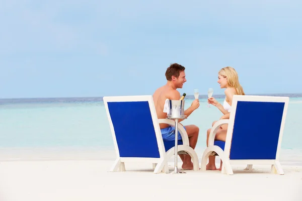 Paar am Strand entspannt sich in Liegestühlen und trinkt Champagner lizenzfreie Stockbilder