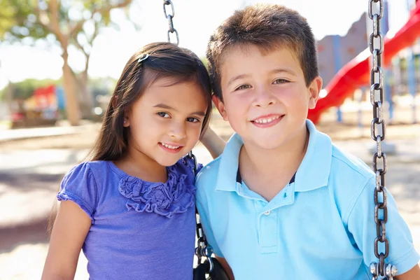 Ragazzo e ragazza giocare su swing in parco — Foto Stock