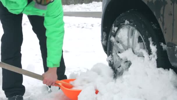 Homem cavando neve ao redor da roda de um carro . — Vídeo de Stock