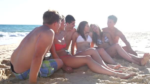 Groep van jeugdvrienden zittend op strand — Stockvideo