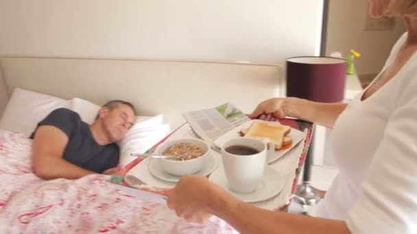 Kobieta kładzie tacę ze śniadaniem przed człowiekiem w łóżku. — Wideo stockowe