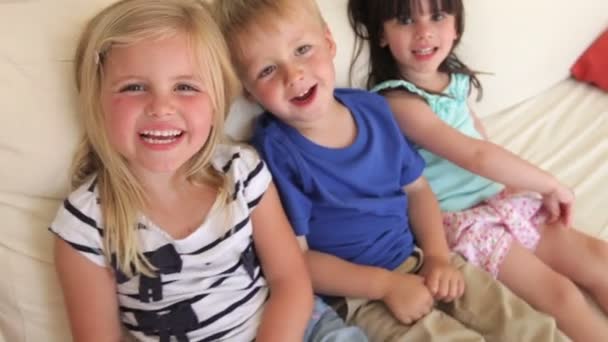 Группа из трех детей сидит на диване — стоковое видео