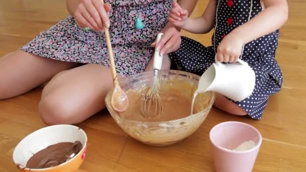 Madre e hija sentadas en el suelo agregando ingredientes en el tazón y mezclando . — Vídeos de Stock