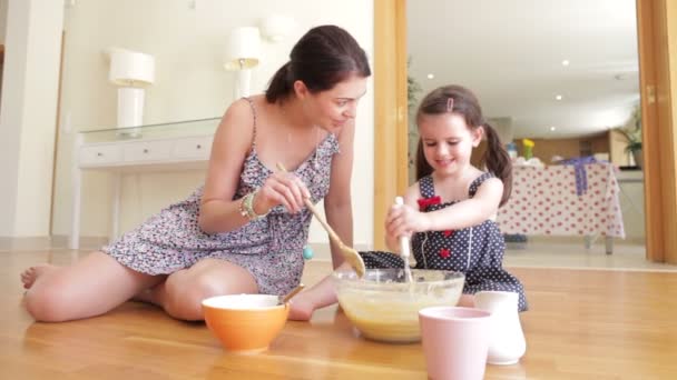 Mother and daughter sitting on floor adding ingredients into bowl and mixing. — Stock Video