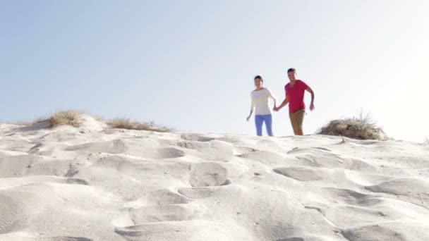 Couple in casual clothing running down sand dune — Stock Video