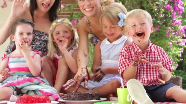 Kinder sitzen am Tisch und essen Schokoladenkuchen mit den Händen - Mütter machen mit. — Stockvideo