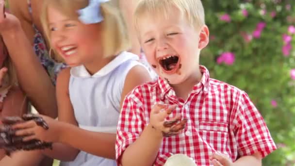 Kinder sitzen am Tisch und essen mit den Händen geschmolzene Schokolade und unterhalten sich mit Freunden. — Stockvideo