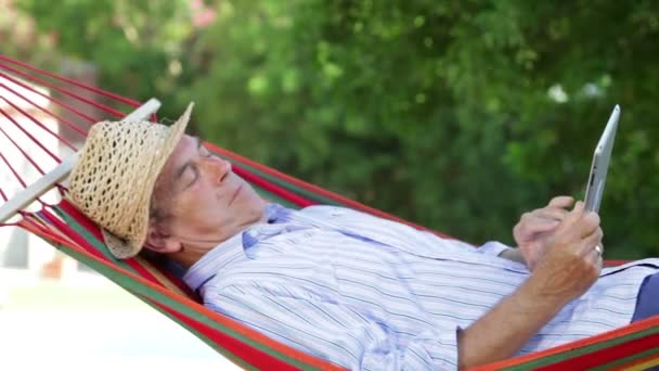 Senior man schommelen in hangmat met behulp van digitale Tablet PC. — Stockvideo