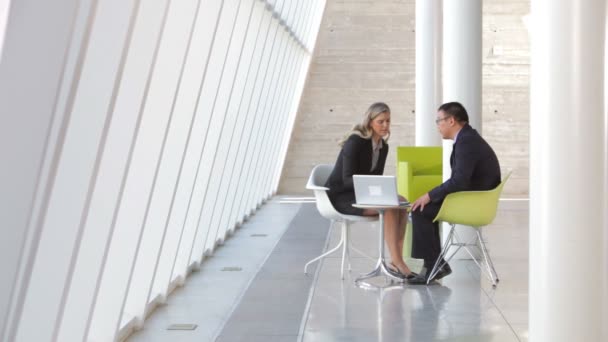 Podnikatel a podnikatelka sedět u stolu v moderní kanceláři společně při pohledu na notebook. — Stock video
