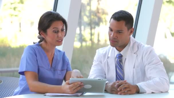 Médico y enfermera sentados en la mesa y dicussing datos en tableta digital . — Vídeo de stock