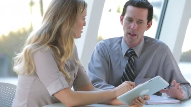 Businessman and businesswoman sitting at desk looking at digital tablet together. — Stock Video