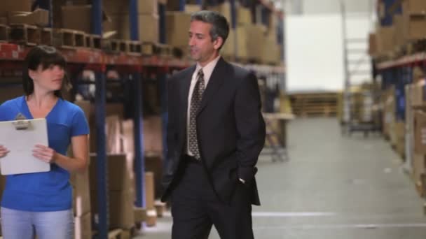 Manager walking in warehouse, talks with worker checking goods on clipboard — Stock Video