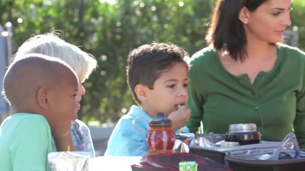 Niños comiendo su almuerzo empacado siendo supervisados por el maestro — Vídeos de Stock