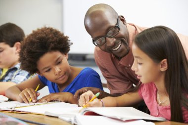 Teacher Helping Pupils Studying At Desks In Classroom clipart