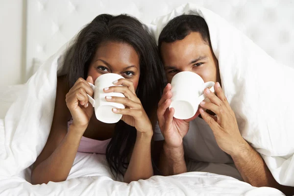 Pareja relajante en la cama con bebida caliente — Foto de Stock