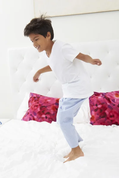 Menino pulando na cama vestindo pijamas — Fotografia de Stock