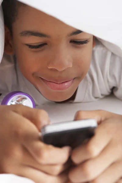 Menino usando telefone celular sob edredão — Fotografia de Stock