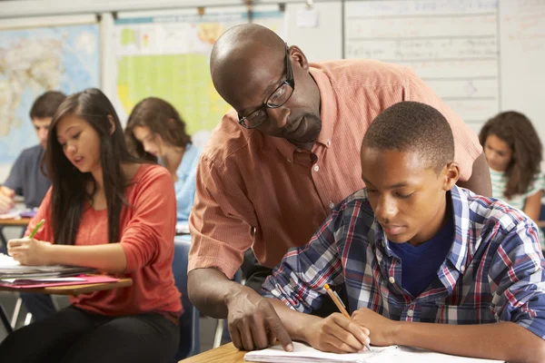 Leraar helpen mannelijke leerling studeren aan Bureau in klas — Stockfoto