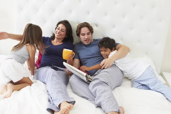 Οικογένεια χαλαρώνοντας σε κρεβάτι με καφέ και εφημερίδα — Φωτογραφία Αρχείου