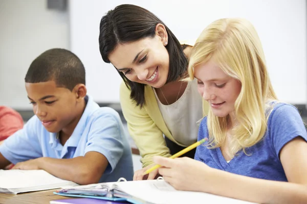 Profesor ayudando a los alumnos a estudiar en los escritorios en el aula — Foto de Stock