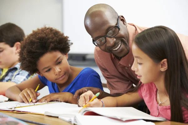 Leraar helpt leerlingen studeren aan bureaus in klas — Stockfoto