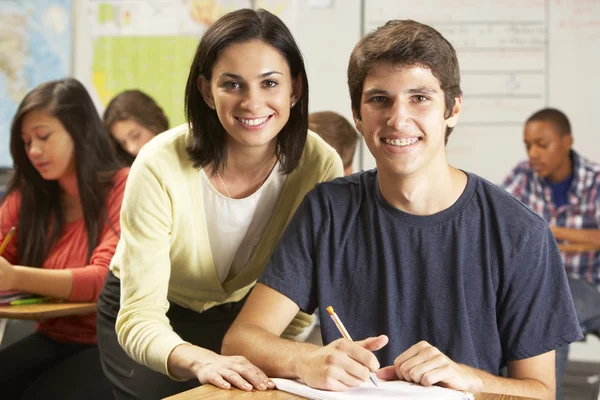 Insegnante che aiuta gli alunni maschi a studiare alla scrivania in classe Fotografia Stock