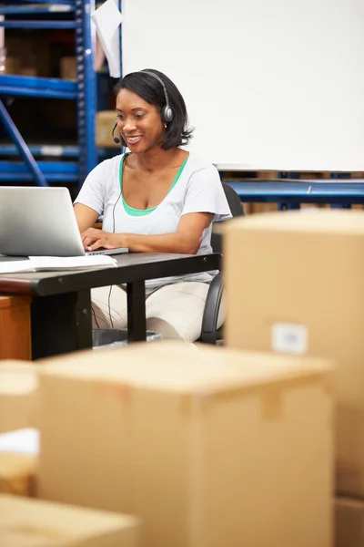 Werknemer in magazijn dragen van hoofdtelefoon en met behulp van laptop — Stockfoto