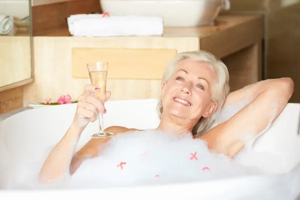 Старшая женщина отдыхает в ванной, пьет шампанское — стоковое фото