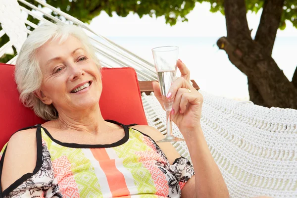 Senior vrouw ontspannen in strand hangmat met champagne — Stockfoto