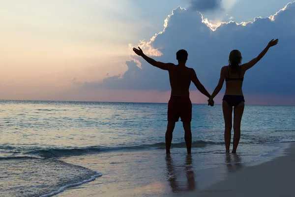 Silhueta de casal andando ao longo da praia ao pôr do sol — Fotografia de Stock