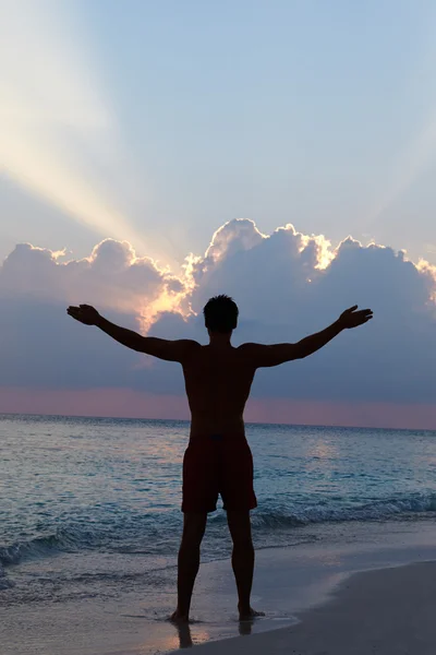 Silueta del hombre con los brazos extendidos en la playa al atardecer — Foto de Stock