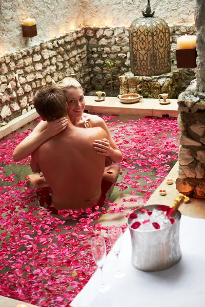 Casal relaxante na piscina coberta de pétalas de flor no spa — Fotografia de Stock