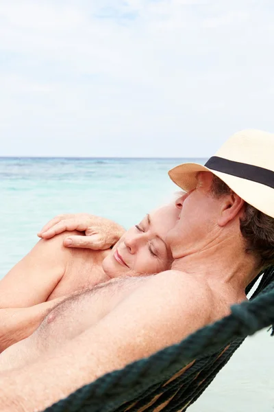 Пара пожилых людей отдыхает в гамаке на пляже — стоковое фото