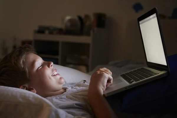 Boy použití přenosného počítače v posteli v noci — Stock fotografie