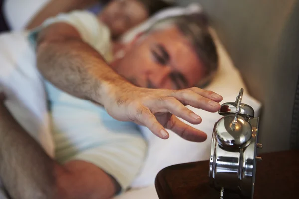 Hombre alcanzando para apagar el reloj de alarma — Foto de Stock