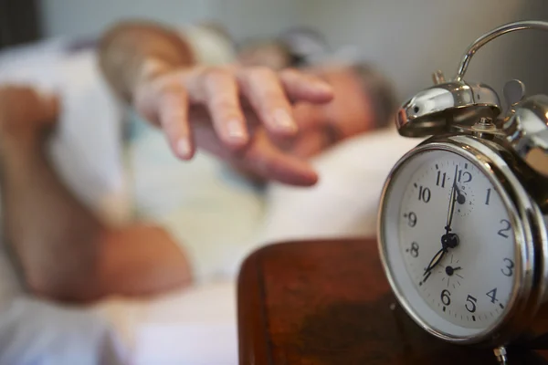 Hombre alcanzando para apagar el reloj de alarma — Foto de Stock