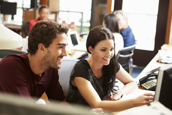 Two Colleagues Working At Desk With Meeting In Background — Stock Photo, Image