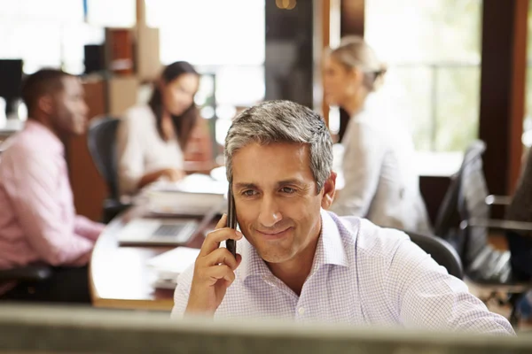 Uomo d'affari al telefono alla scrivania con riunione in background — Foto Stock