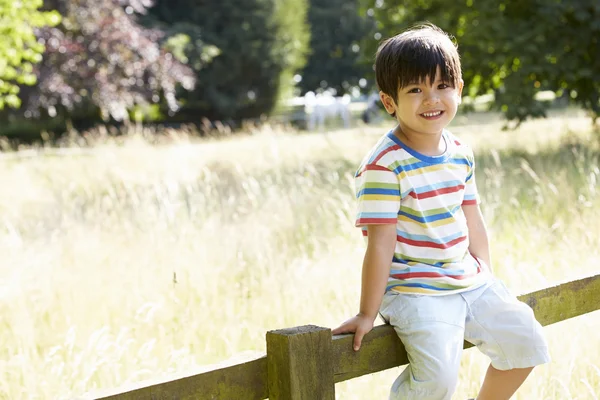 Asiatico ragazzo seduta su recinto in campagna — Foto Stock