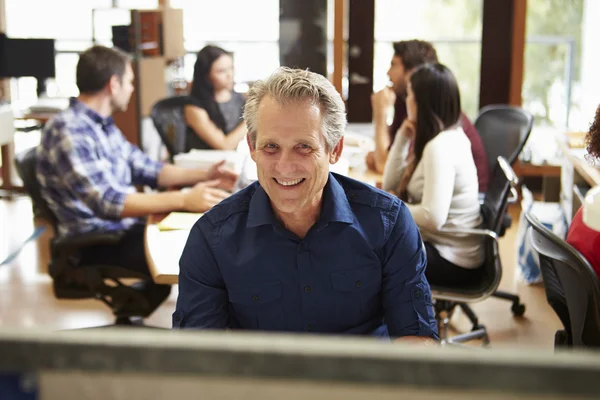 Geschäftsmann arbeitet am Schreibtisch mit Meeting im Hintergrund — Stockfoto