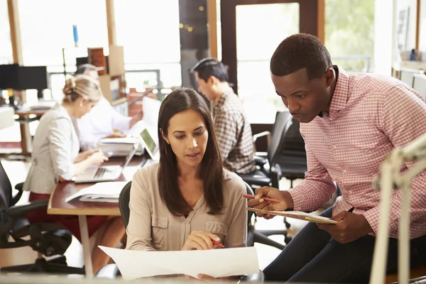 Twee collega's werken aan bureau met vergadering in achtergrond — Stockfoto