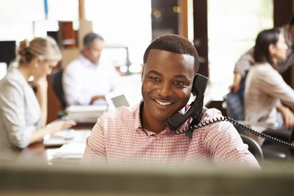 Бизнесмен на телефоне на рабочем столе со встречей в фоновом режиме — стоковое фото