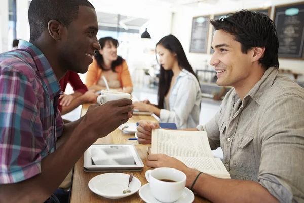 Dos amigos masculinos se reúnen en una cafetería ocupada — Foto de Stock