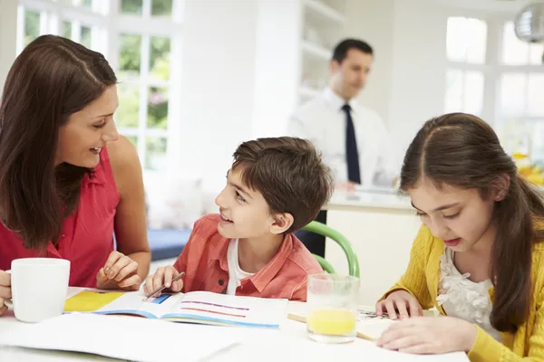 Mamá ayuda a los niños con la tarea mientras papá trabaja en segundo plano — Foto de Stock