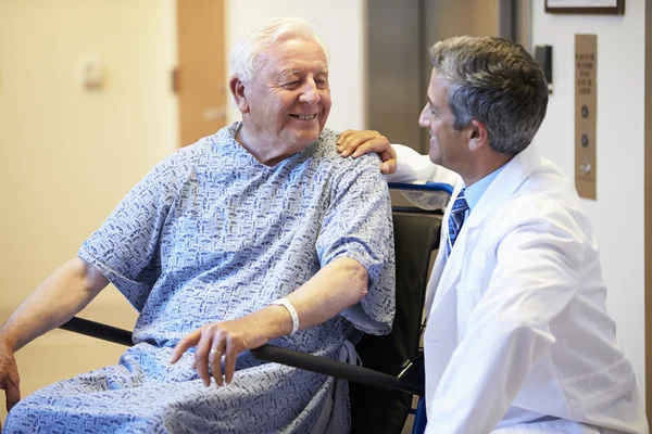 Patient masculin âgé se faisant pousser en fauteuil roulant par un médecin — Photo